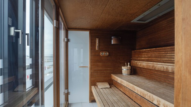 Uma sauna com bancos de madeira, porta de vidro, parede de madeira e um pequeno aquecedor na parede.