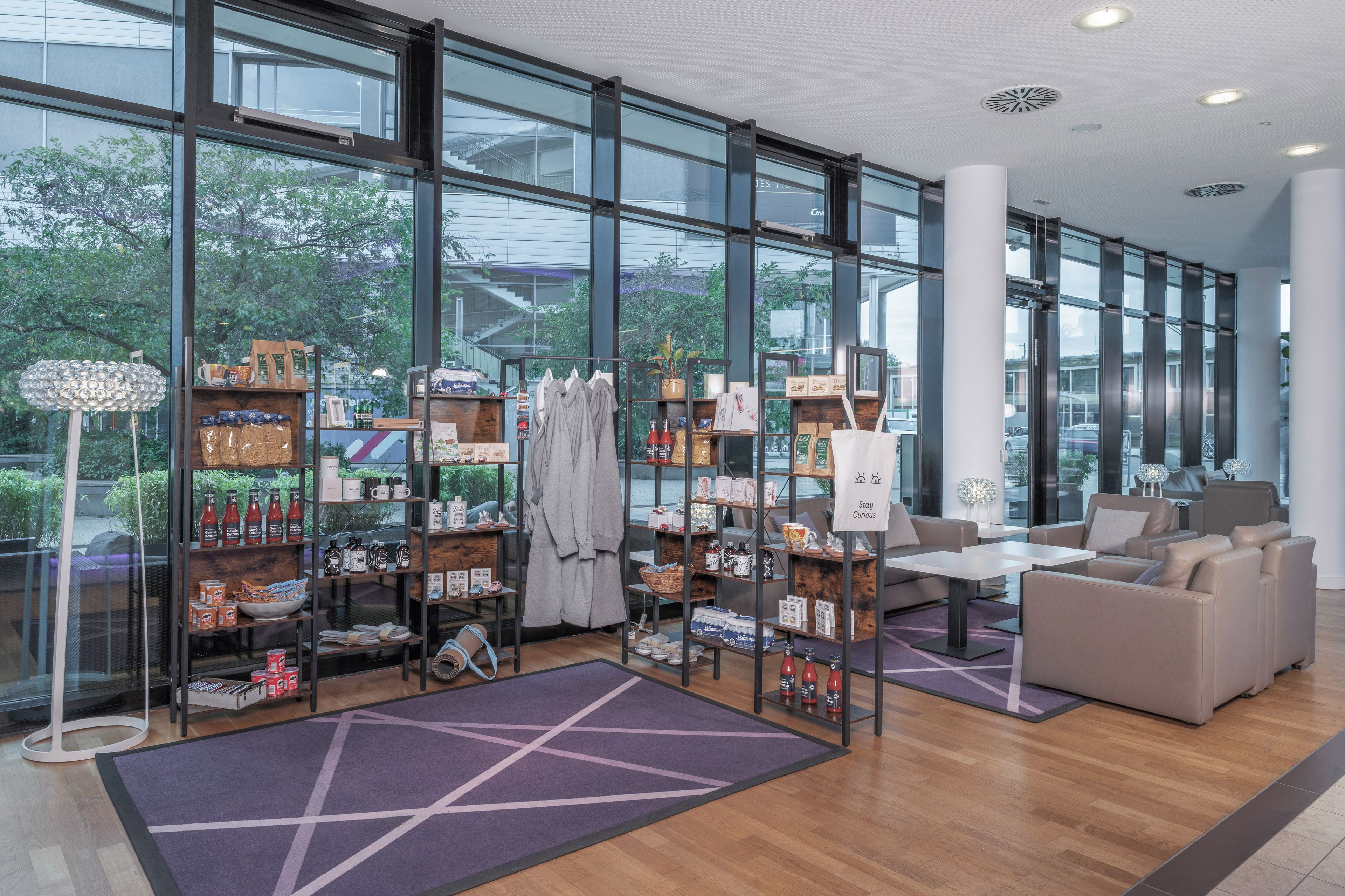 Eine geräumige Lobby mit Sitzgelegenheit, einer Kaffeestation und Blick ins Freie durch große Fenster.