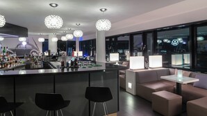 Uma área de bar moderna com uma ilha central, banquetas e iluminação ambiente.