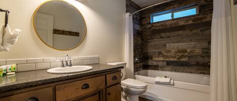 A bathroom with a wooden wall, a round mirror, a sink, a toilet, and a bathtub.