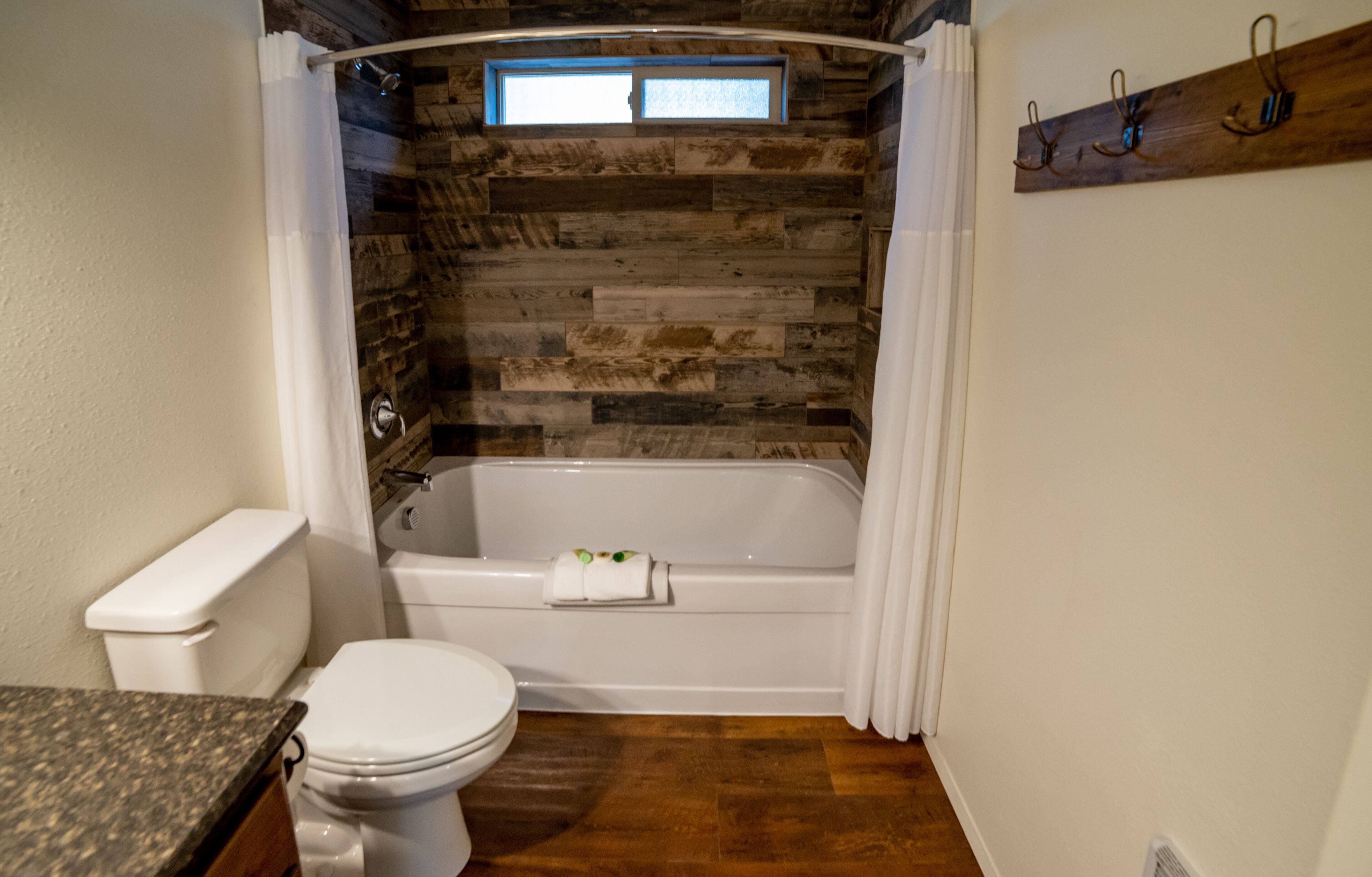 A bathroom with a stone wall, a bathtub, a toilet, and a window.