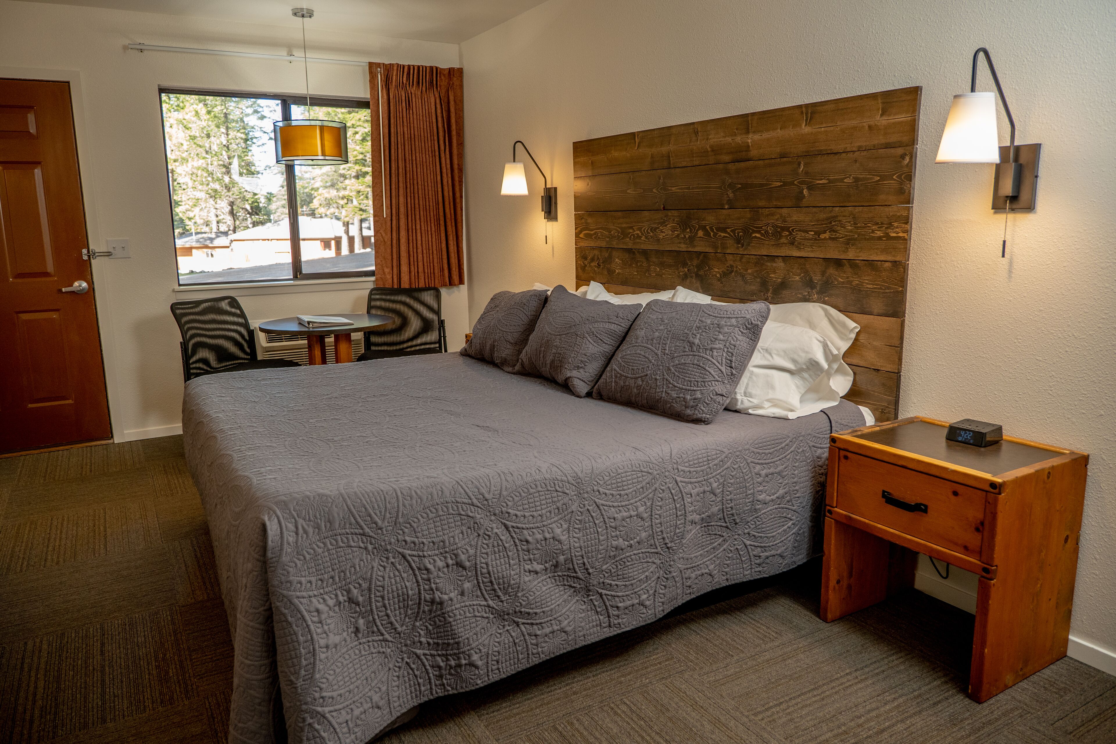 A neatly arranged bedroom with a large bed, a bedside table, a chair, and a window with curtains.
