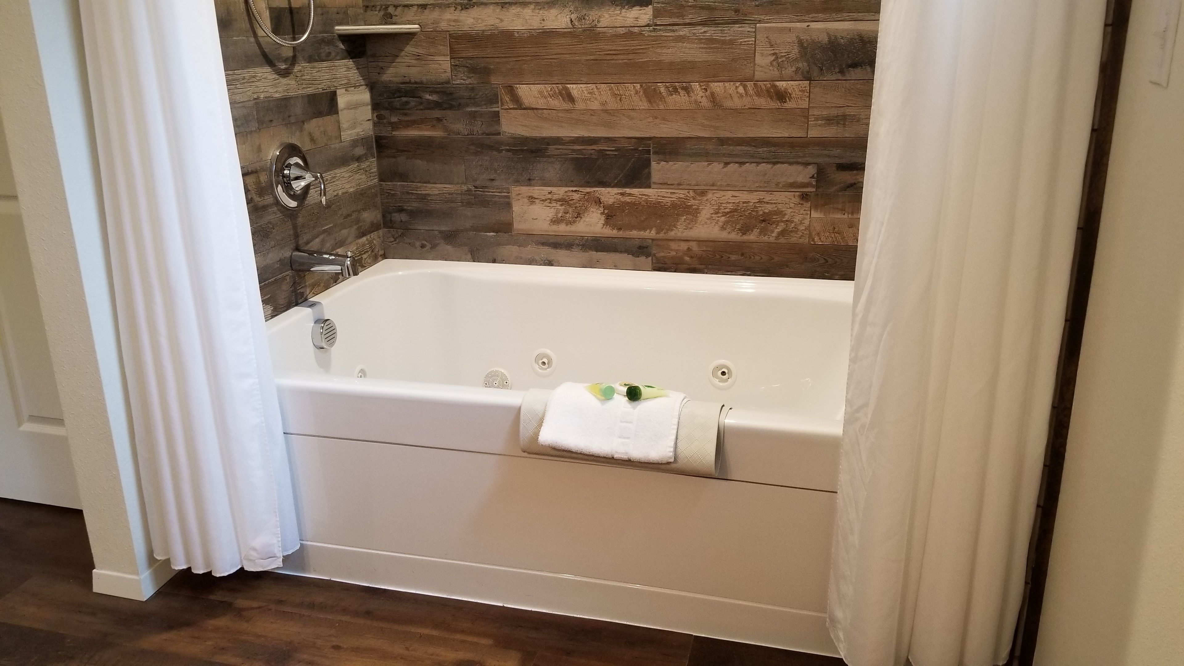 A white bathtub with a towel, set against a wooden wall.