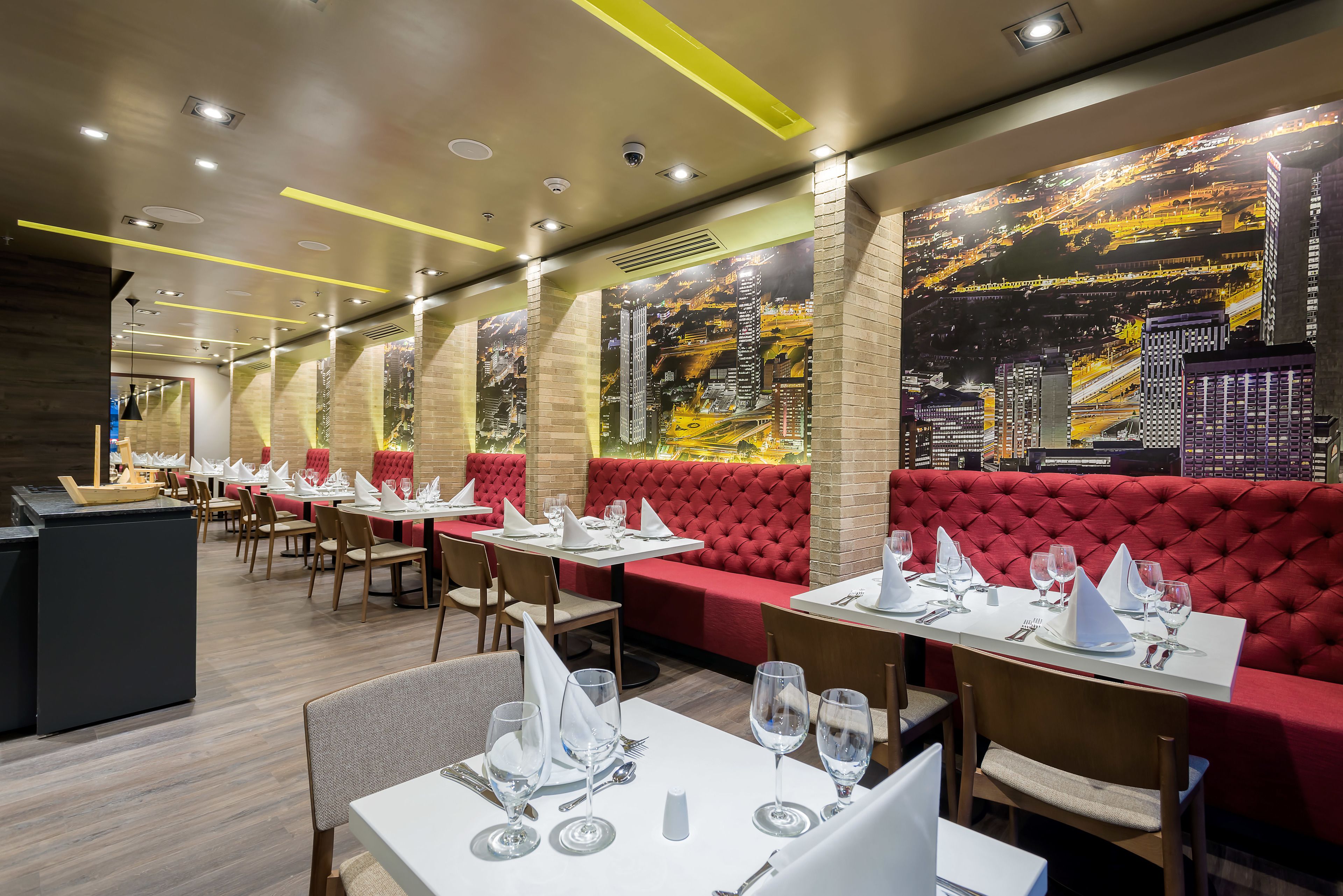 En restaurang med bord uppdukade för middag, röda, vadderade sittplatser och en väggmålning som föreställer stadens silhuett.