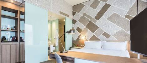 A hotel room with a bed, desk, chair, and a wall with a geometric pattern.