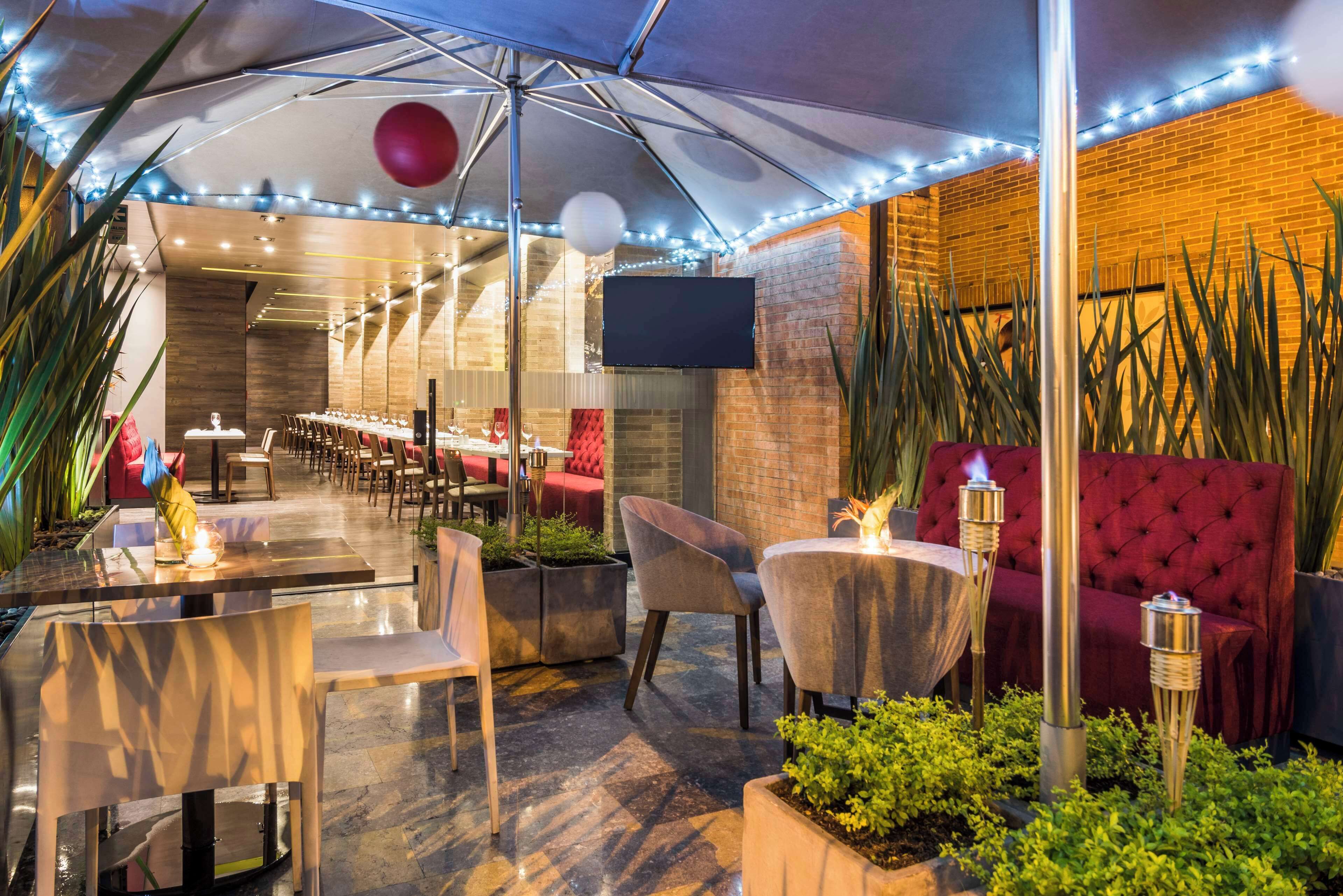 An outdoor dining area with tables and chairs, a red sofa, and decorative lighting.
