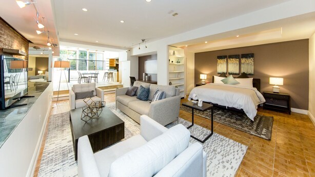 A modern hotel room with a large bed, a sofa, a dining area, and a kitchen in the background. - Chelsea Pines Inn (New York)