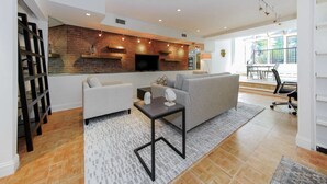 A modern living room with a brick accent wall, a flat-screen TV, a grey sofa, and a coffee table. - Chelsea Pines Inn (New York)