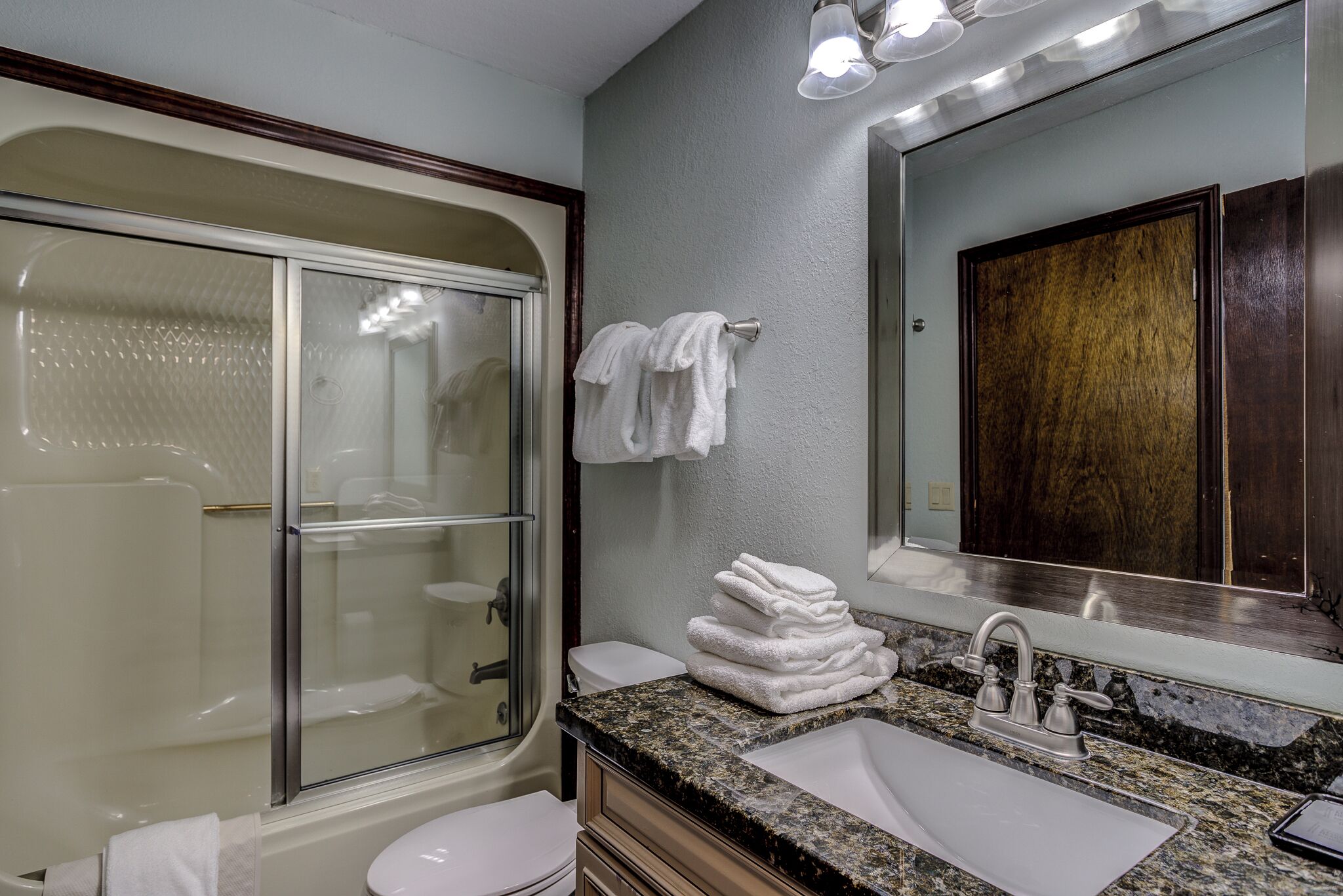 A bathroom with a glass-enclosed shower, a sink with a marble countertop, and a large mirror with a wooden cabinet.