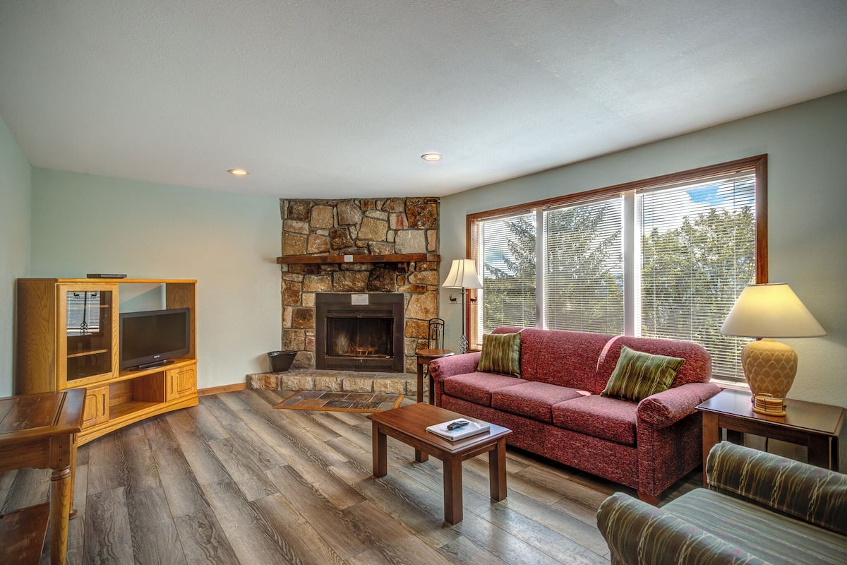 A living room with a stone fireplace, a red sofa, a wooden coffee table, and a television on a wooden stand.