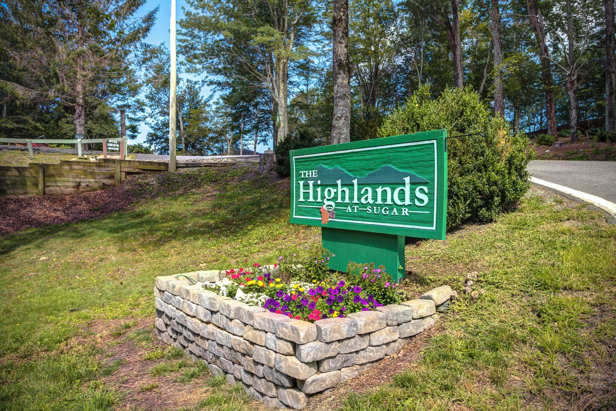 A sign for "The Highlands at Sugar" with a stone planter and flowers.