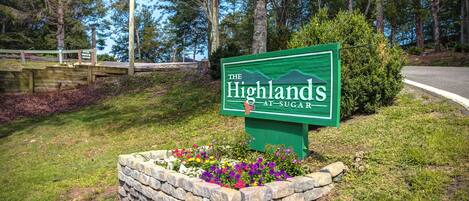 A sign for "The Highlands at Sugar" with a stone planter and flowers.