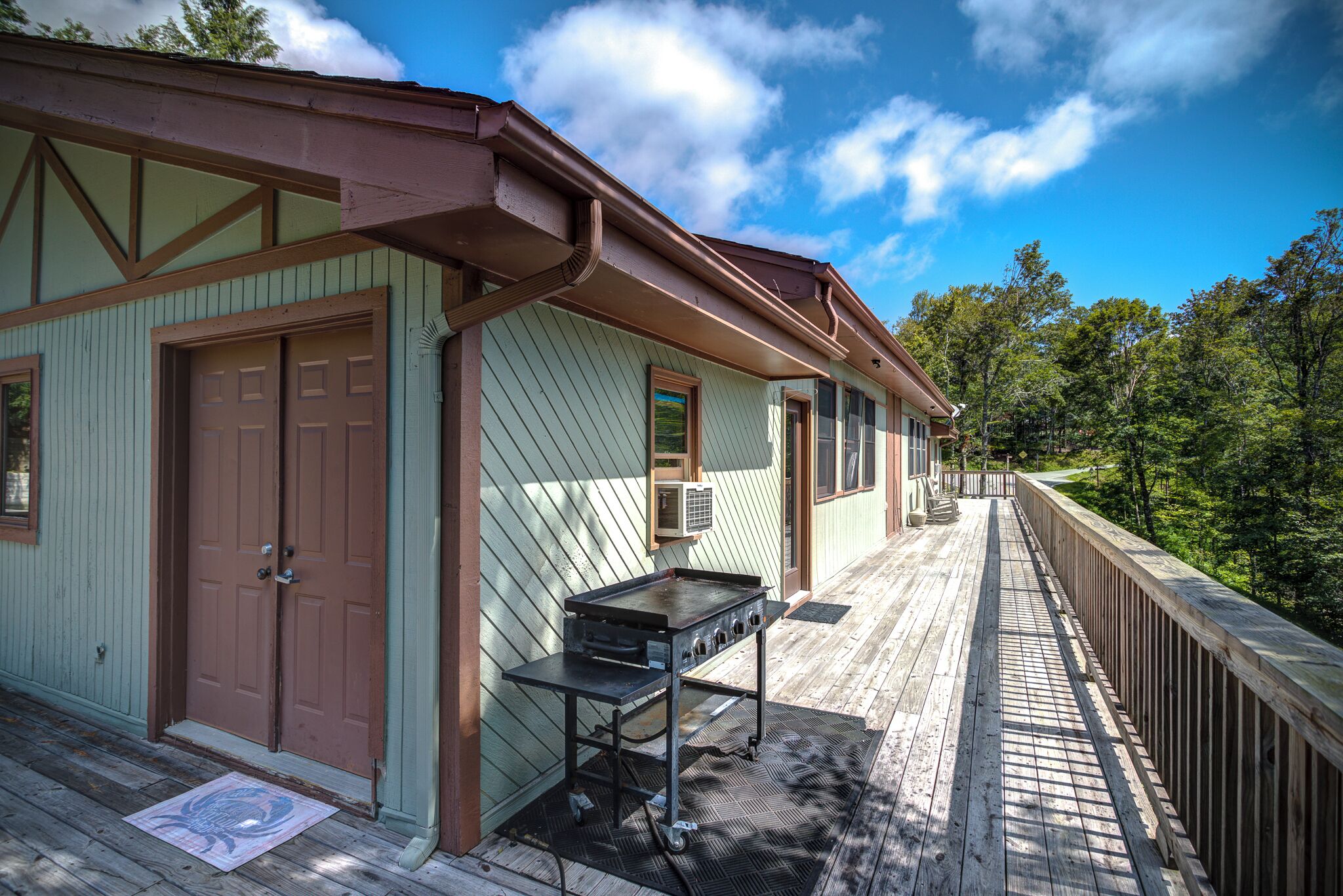 A wooden deck with a grill and a door to a building.