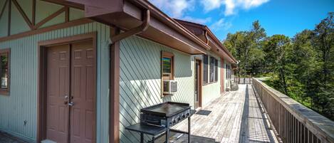 A wooden deck with a grill and a door to a building.