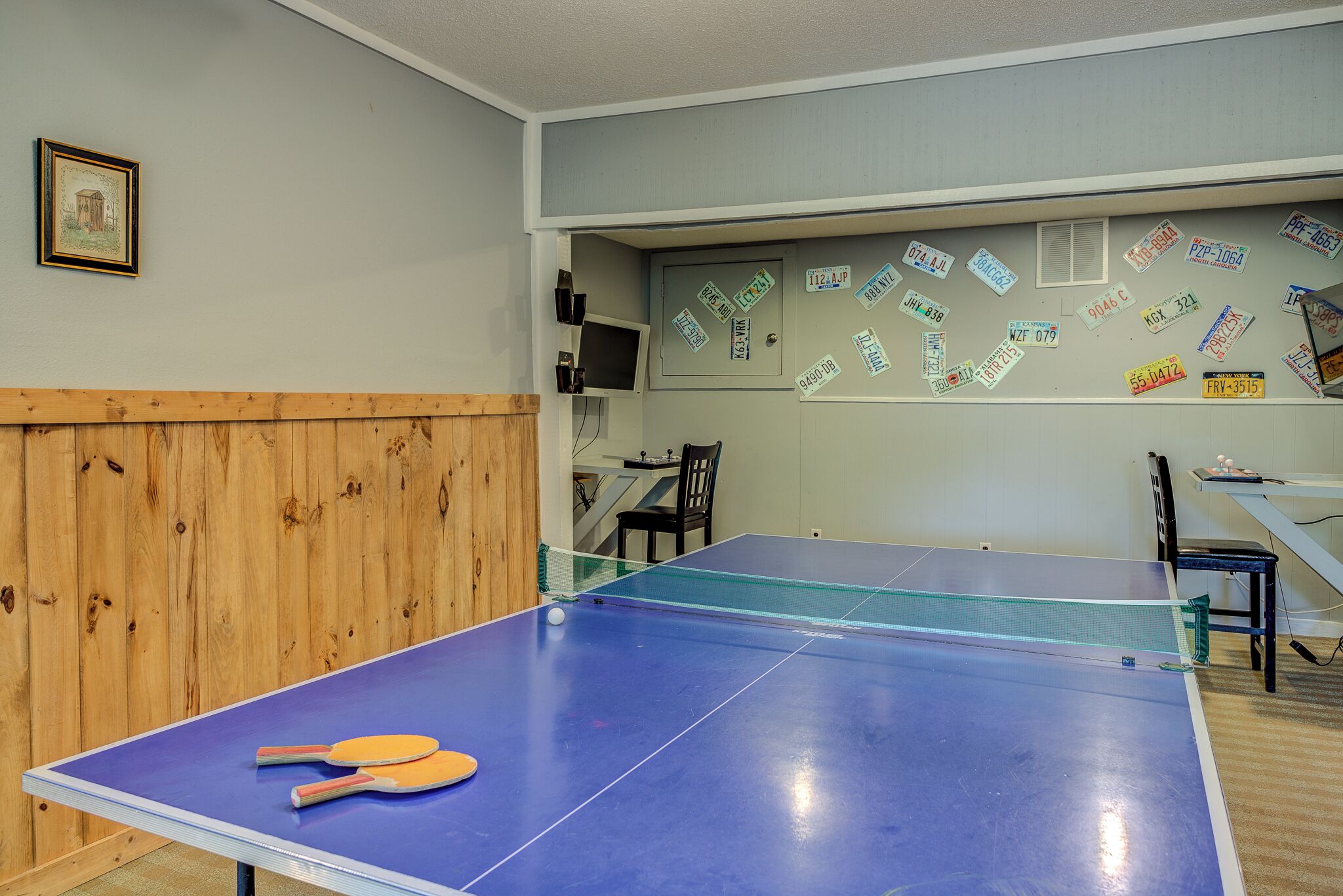 Une pièce équipée d’une table de ping-pong, de chaises, d’un mur recouvert de panneaux de bois et d’un autre mur décoré de divers autocollants.