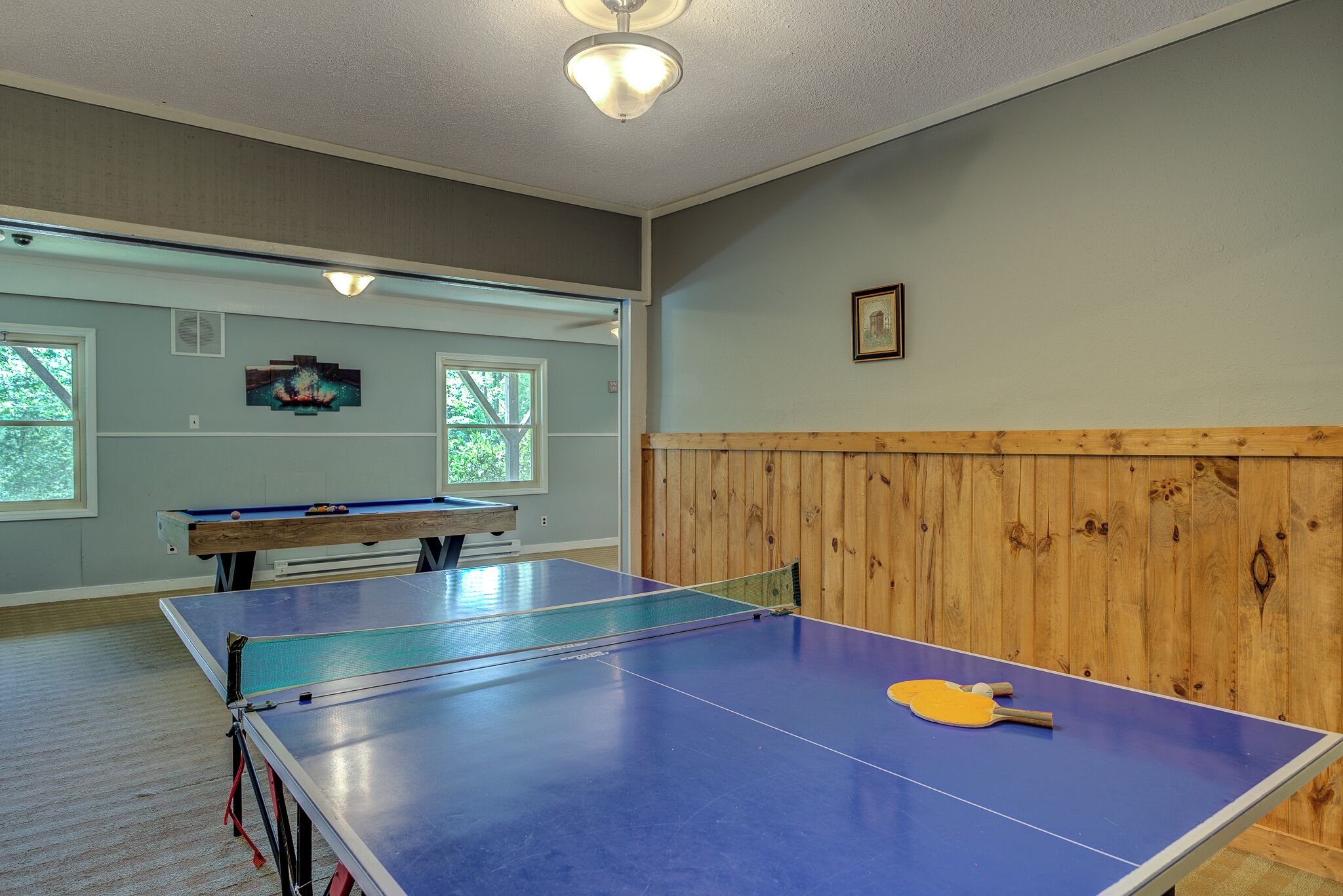 A room with a ping pong table, a pool table, and a wooden panel wall.
