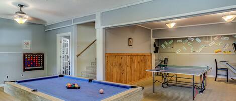 Une table de billard, une table de ping-pong et un porte-billes dans une pièce aux murs lambrés et dotée d’un escalier.