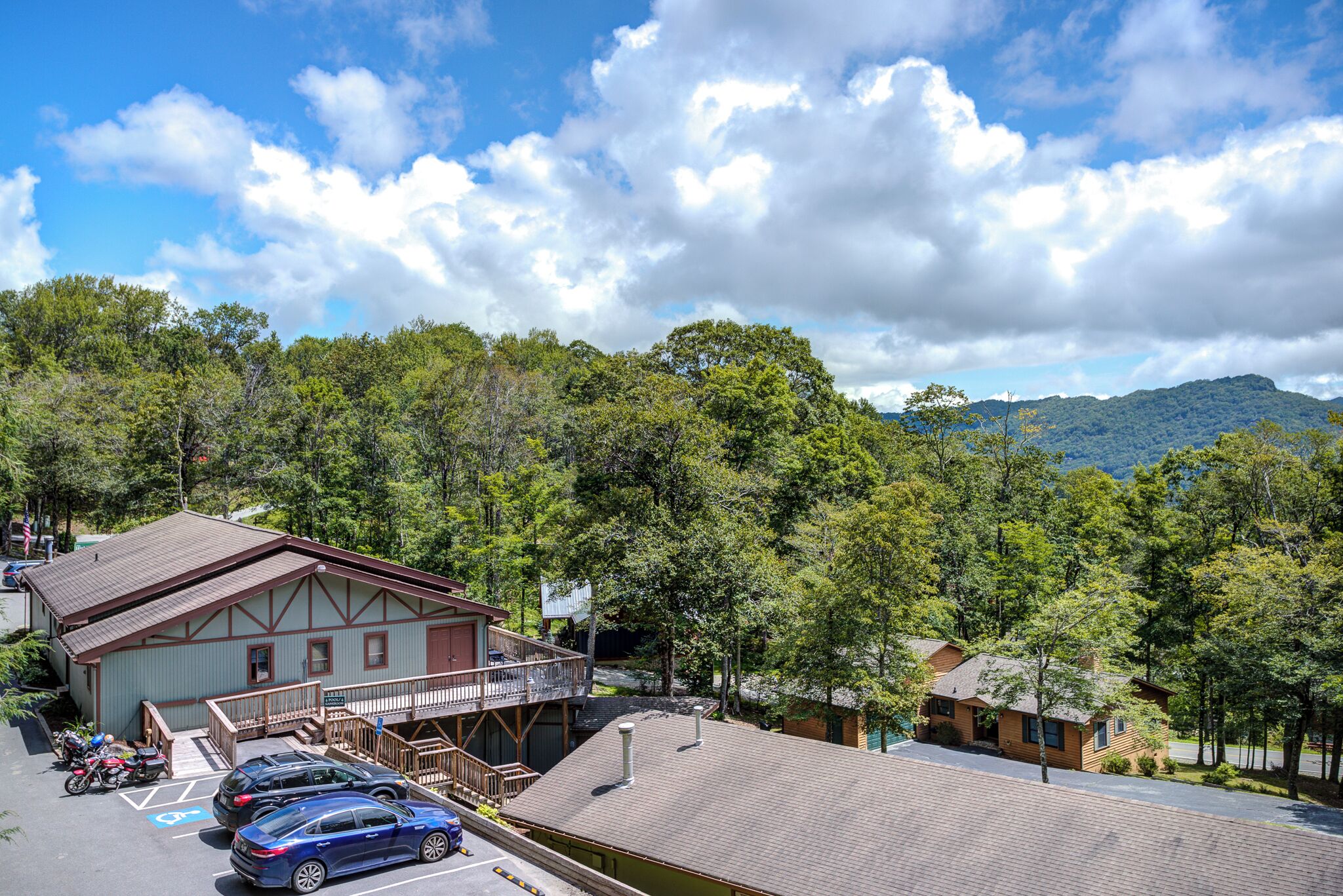 Una cabaña con balcón, zona de estacionamiento y vista a una montaña boscosa.