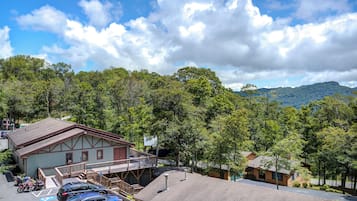 A lodge with a balcony, parking area, and a view of a forested mountain.
