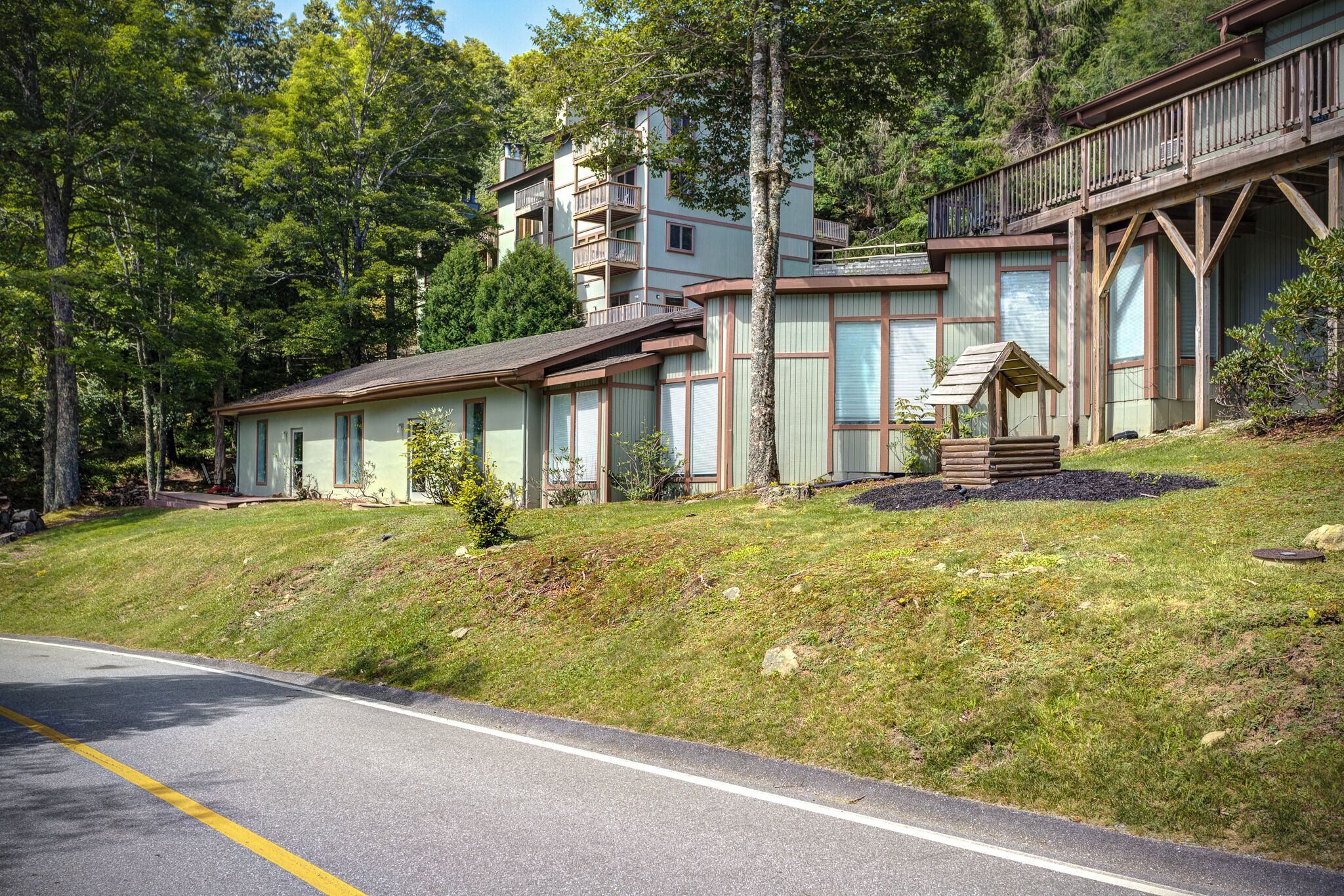 A two-story building with a wooden deck and a small wooden structure on the front lawn.