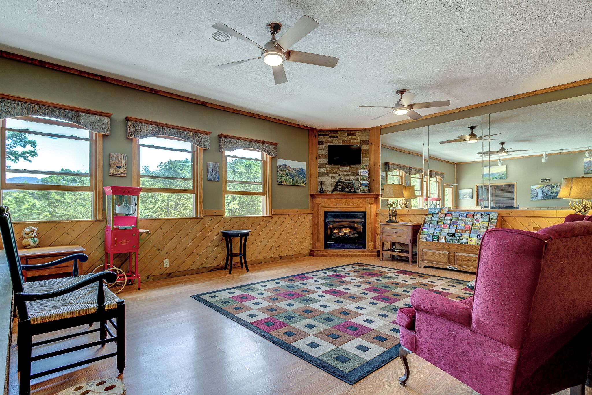 A cozy living room with a fireplace, wooden walls, and large windows.