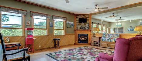 A cozy living room with a fireplace, wooden walls, and large windows.