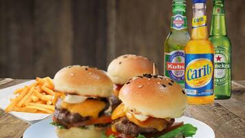 A plate with two burgers and fries, and three beer bottles.