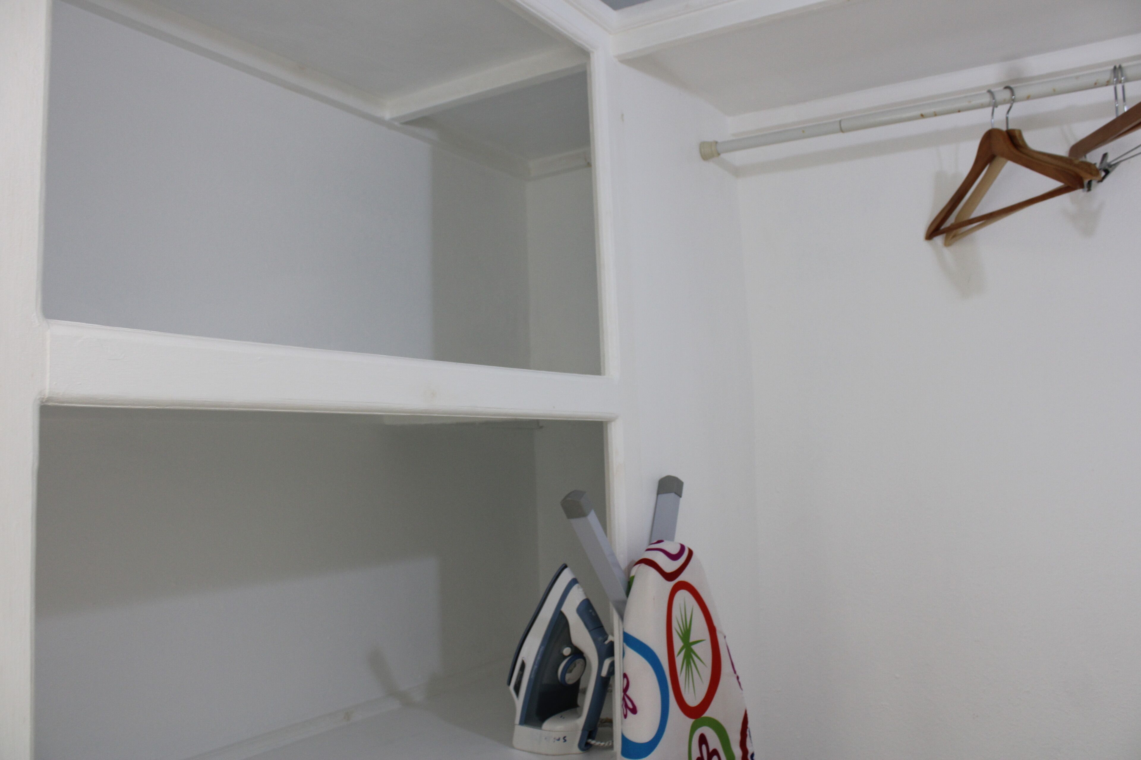 Una habitación con paredes blancas, molduras blancas en el techo y un tendedero con perchas de madera.