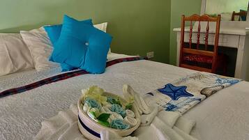 Una cama bien hecha con un almohilar azul, uno blanco y una manta escocesa. Hay una cesta con toallas dobladas y una manta con diseño de estrella de mar sobre la cama.