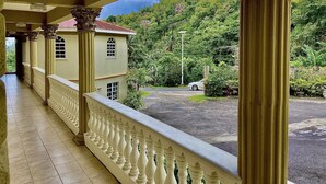 A covered walkway with ornate columns and a balustrade, leading to a building with a red roof.