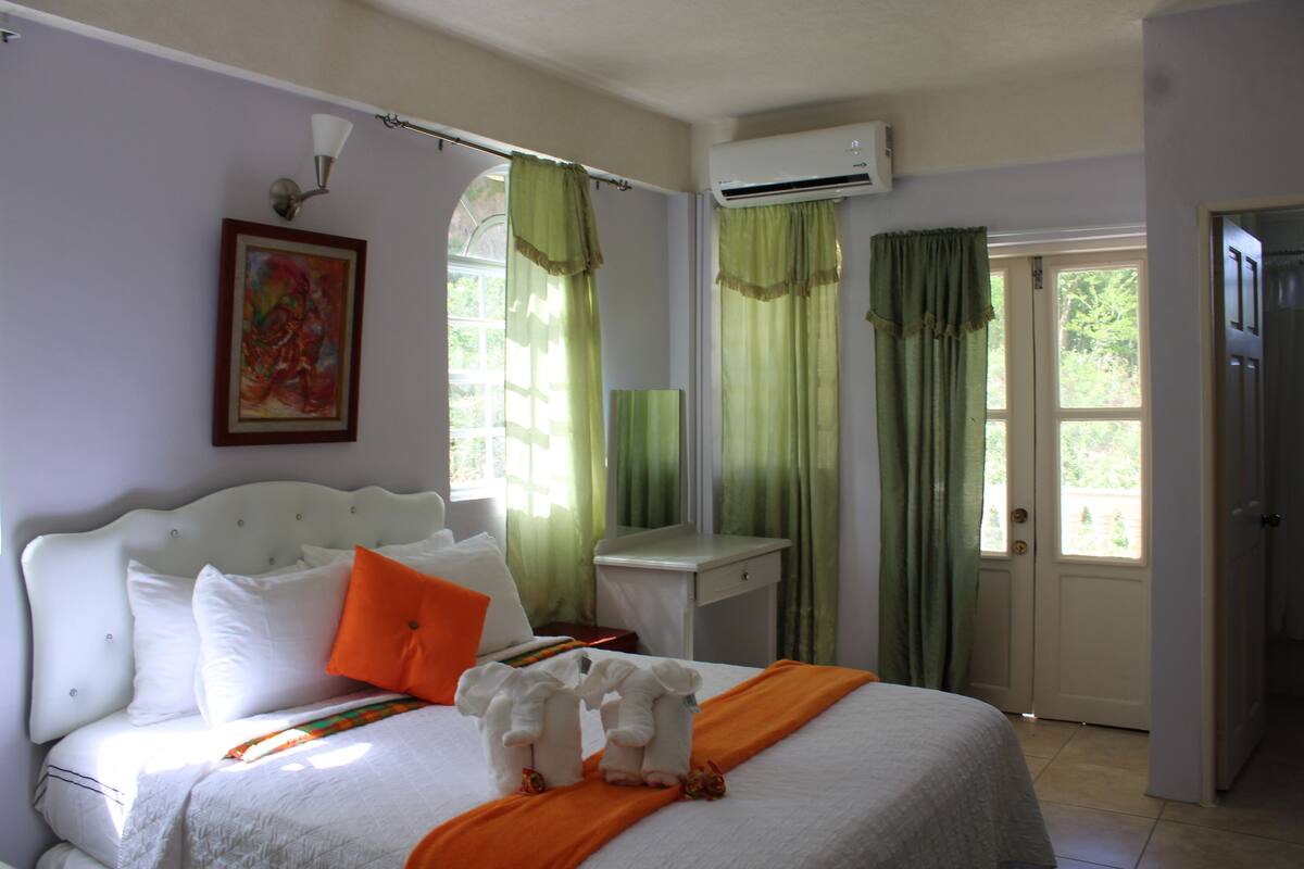 A hotel room with a bed, a nightstand, a window with curtains, and an air conditioning unit.