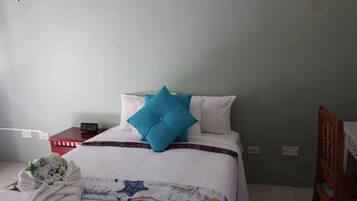 A neatly made bed with a blue pillow, a bedside table with a phone, and a towel on the floor.