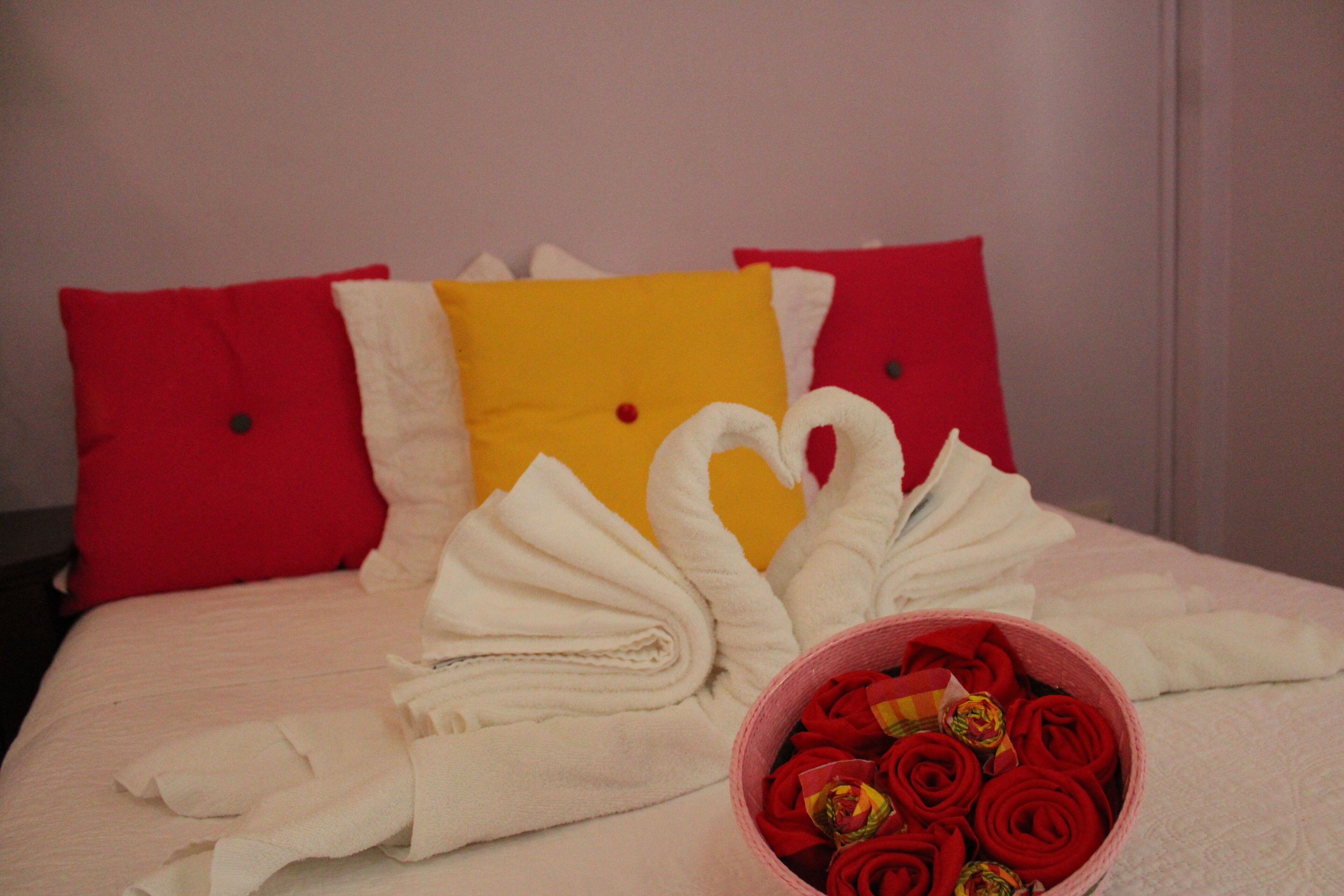 Un lit bien fait, agrémenté d’une décoration en forme de cœur réalisée avec des serviettes et d’un panier rempli de roses rouges.
