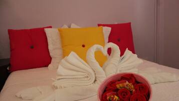 Un lit bien fait, agrémenté d’une décoration en forme de cœur réalisée avec des serviettes et d’un panier rempli de roses rouges.