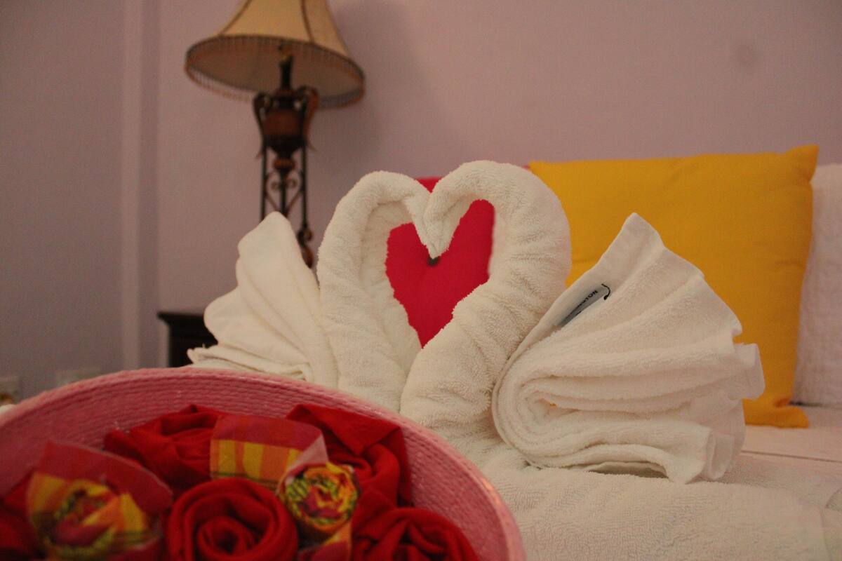 A neatly made bed with a heart-shaped towel and a yellow pillow.