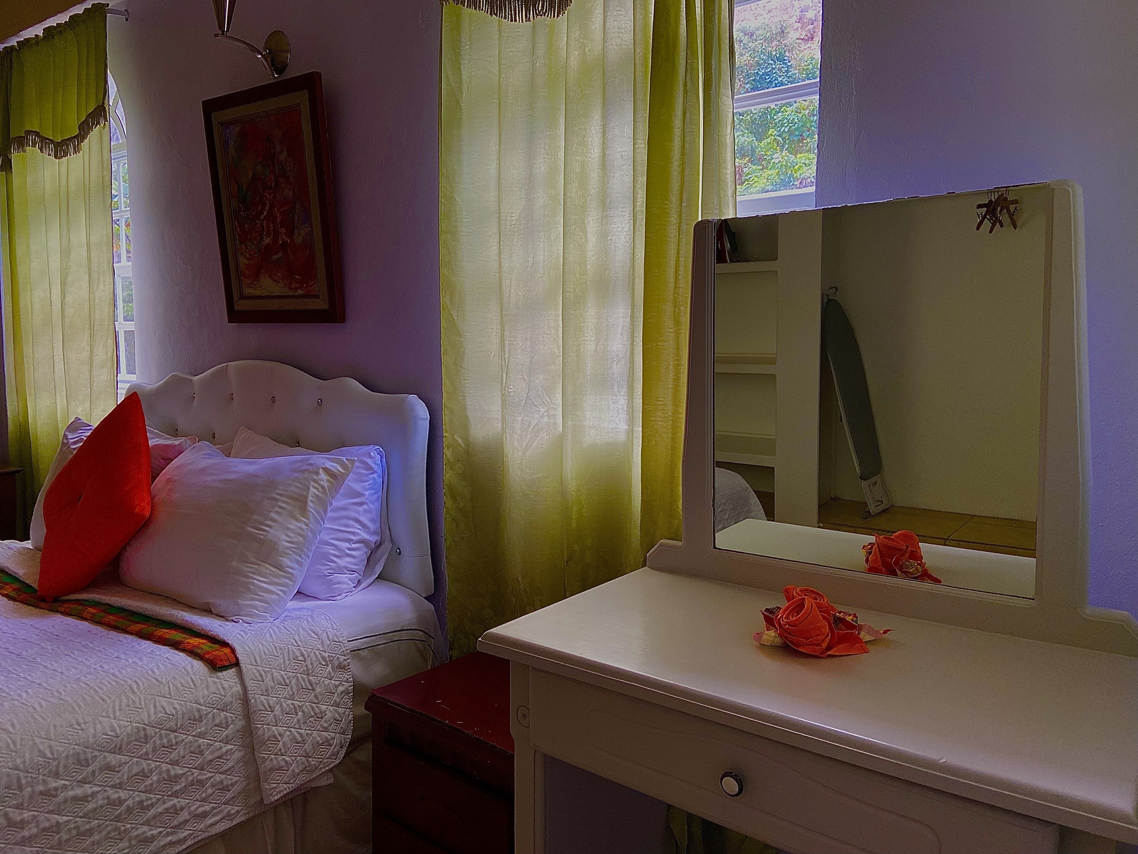 Une chambre à coucher avec un lit, une table de chevet, un miroir et une fenêtre avec des rideaux.