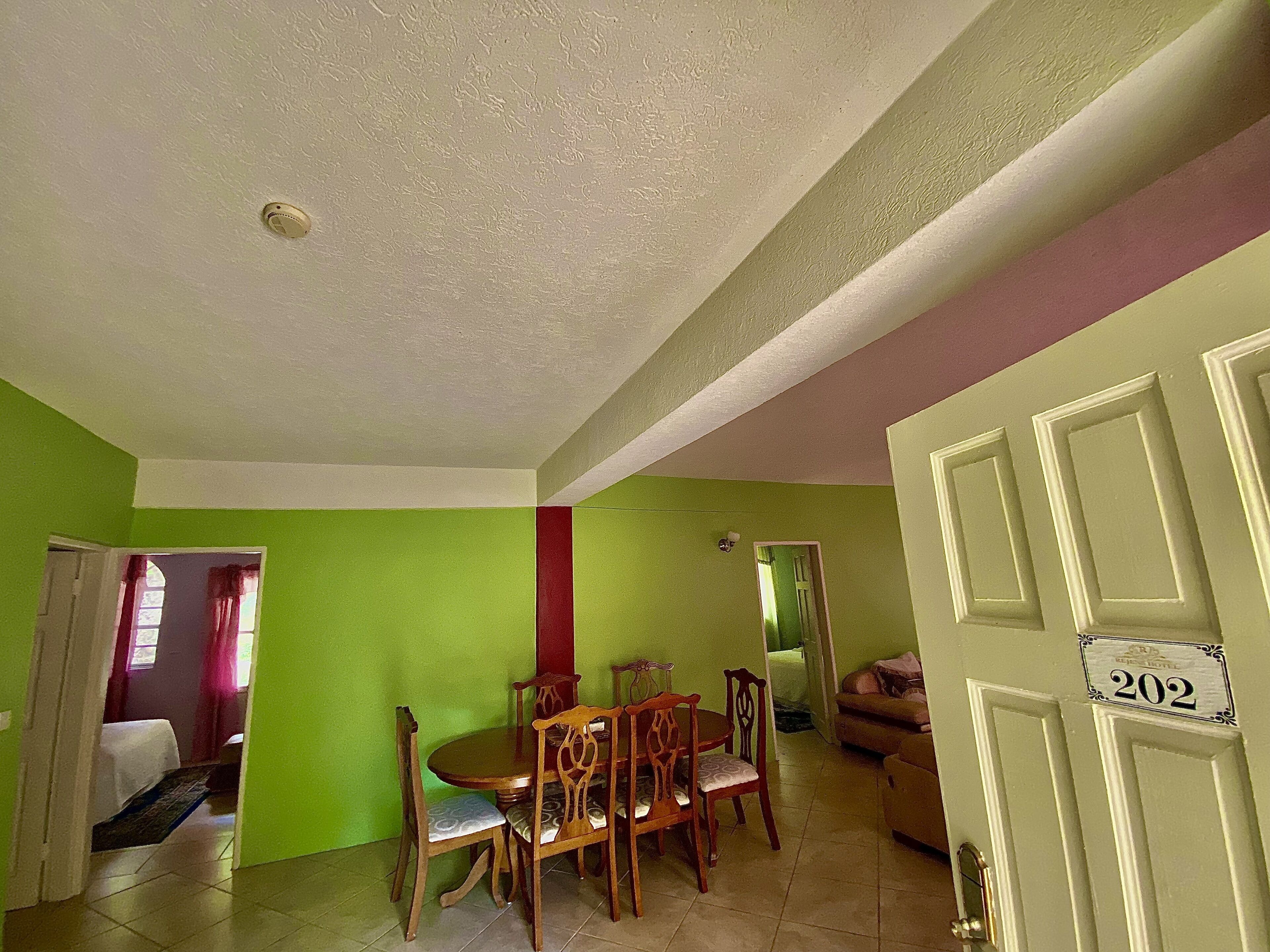A dining area with a wooden table and chairs, a green wall, and a door with the number 202.