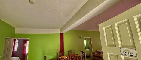 A dining area with a wooden table and chairs, a green wall, and a door with the number 202.