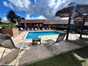 A swimming pool area with lounge chairs, a small table, and a thatched umbrella. - Hotel Antiguo Camino (Villa General Belgrano)