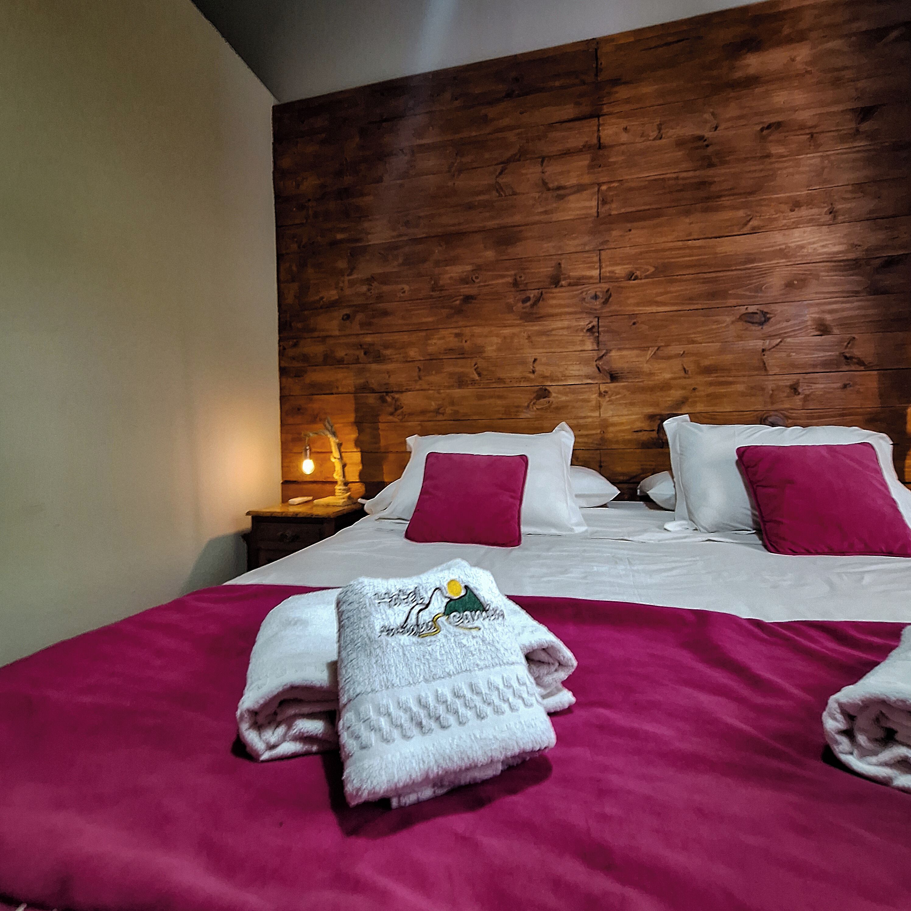 Une chambre d’hôtel avec une tête de lit en bois, un lit bien fait avec une literie blanche et rose, et deux serviettes posées sur le lit.