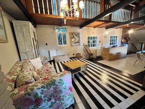 A room with a floral sofa, a wooden coffee table, a black and white striped floor, a white brick wall, and a wooden staircase.