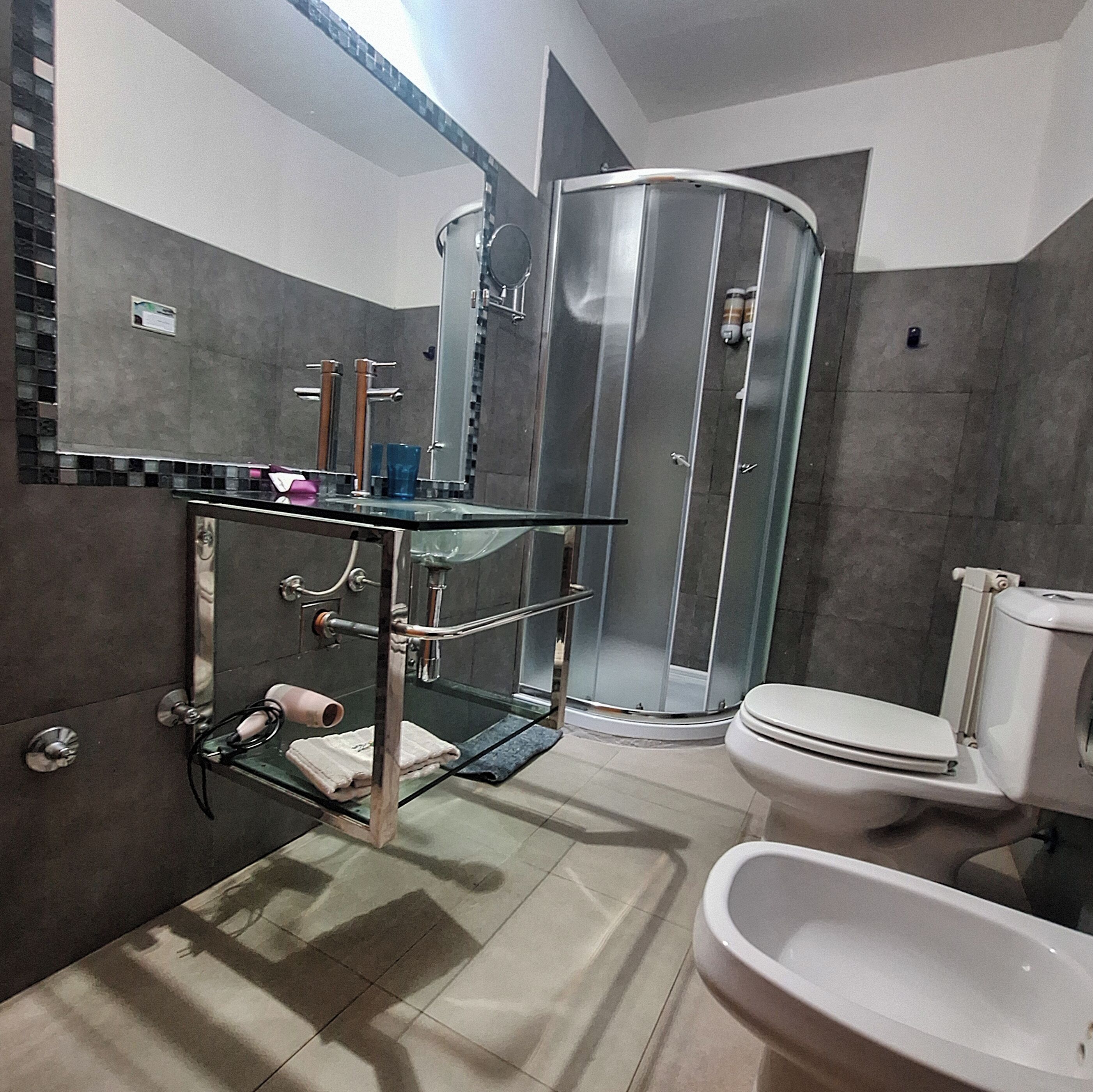 Une salle de bain moderne avec une douche à parois de verre, une étagère en verre où sont rangés les articles de toilette, des toilettes et une baignoire.
