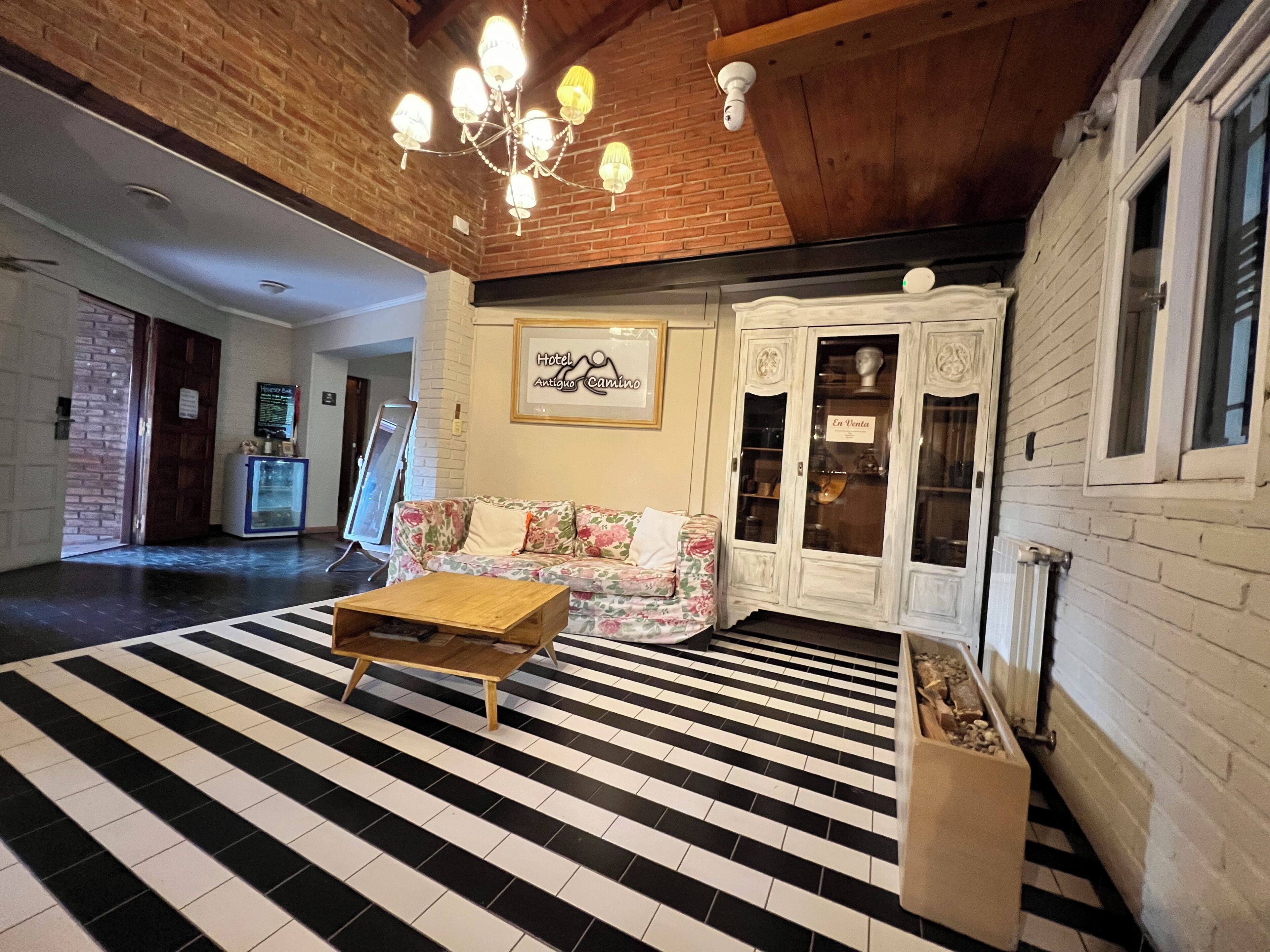 Un vestíbulo de hotel con piso a rayas blanco y negro, una mesa de centro de madera, un sofá floral y una araña.