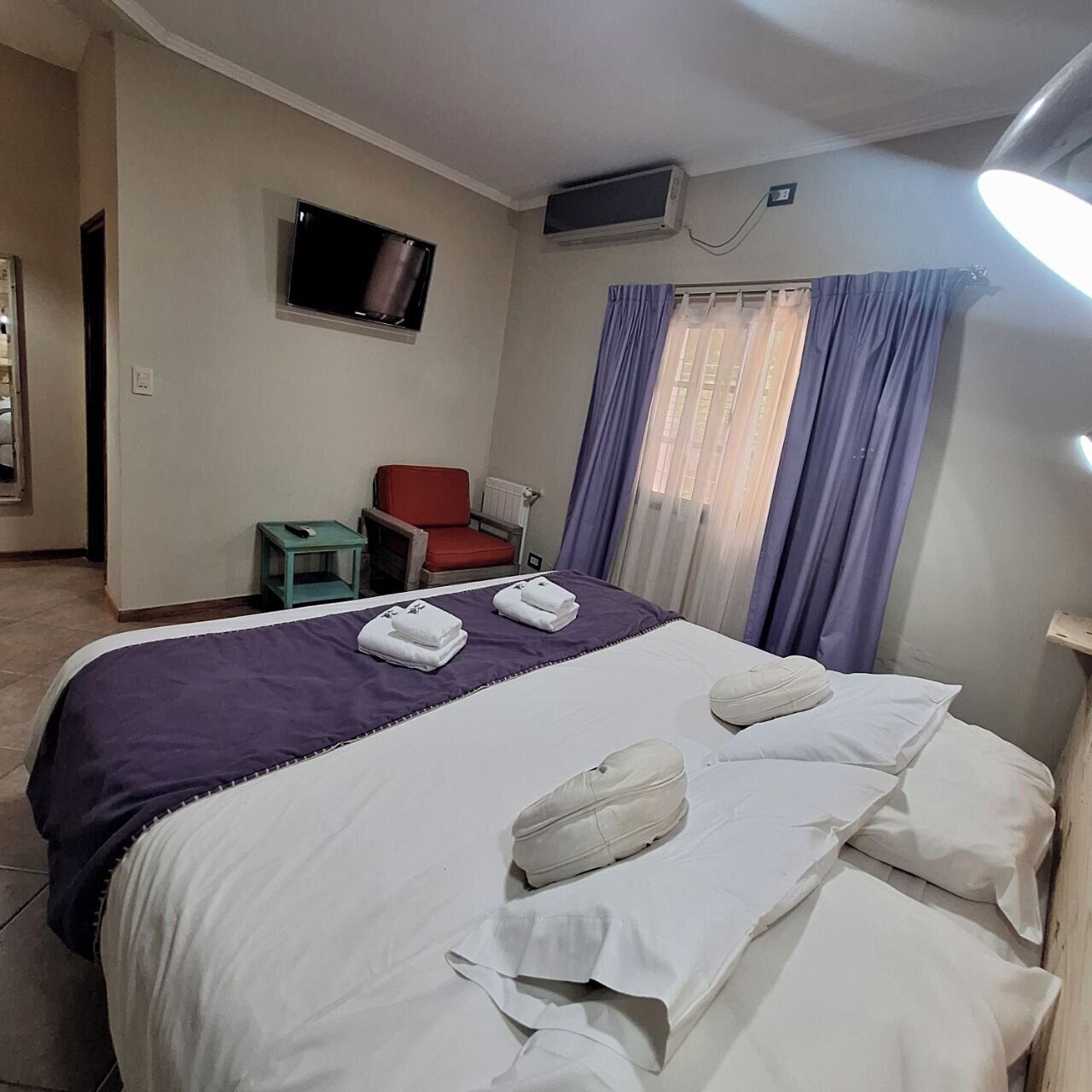 Hotellihuone, jossa on sänky, televisio, tuoli ja pieni pöytä.