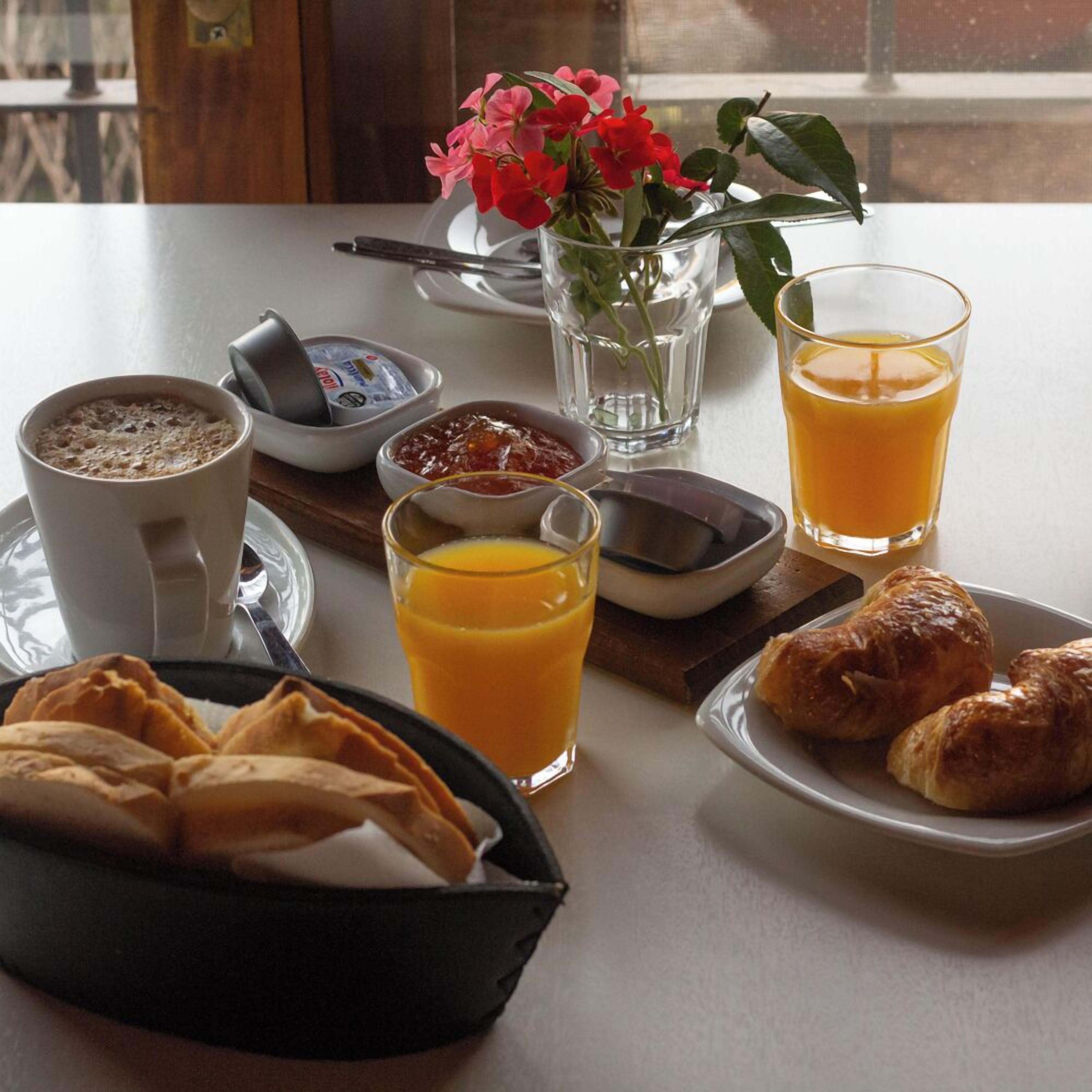 Una mesa de desayuno con una taza de café, jugo de naranja, croissants, mermelada y un florero.