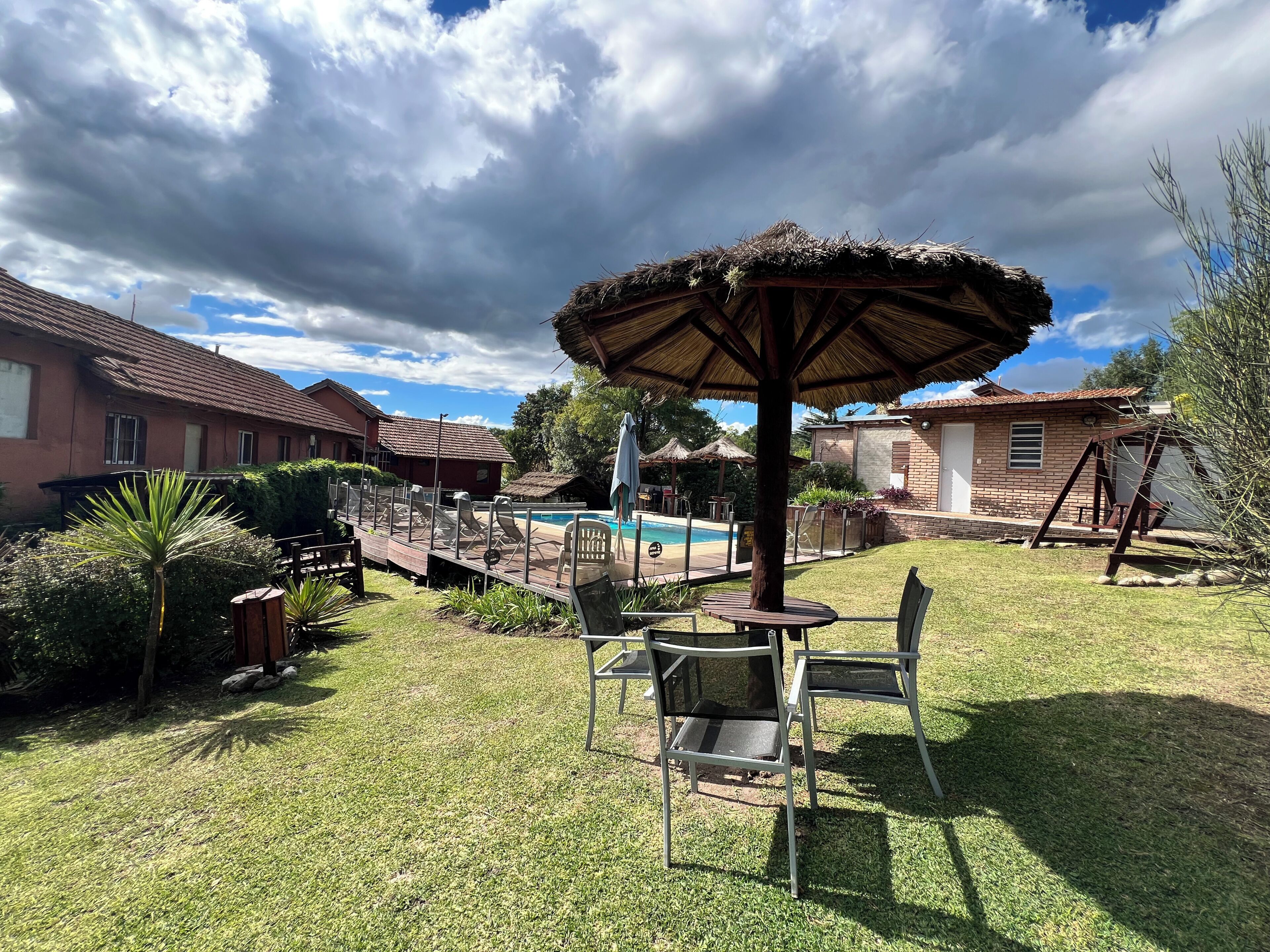 Un patio trasero con piscina, sillones, una mesa y una sombrilla.