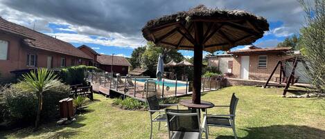 Un patio trasero con piscina, sillones, una mesa y una sombrilla.