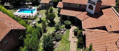 A hotel with a swimming pool, red-tiled roofs, and a garden area.