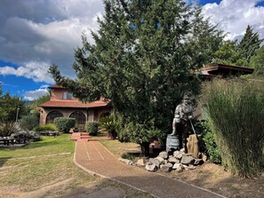 A house with a brick facade, a red-tiled roof, and a pathway leading to a statue.