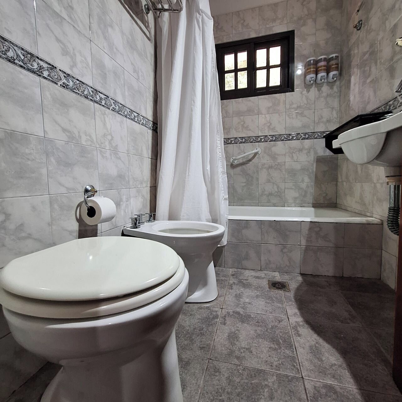 A bathroom with two toilets, a bathtub, and a shower curtain.